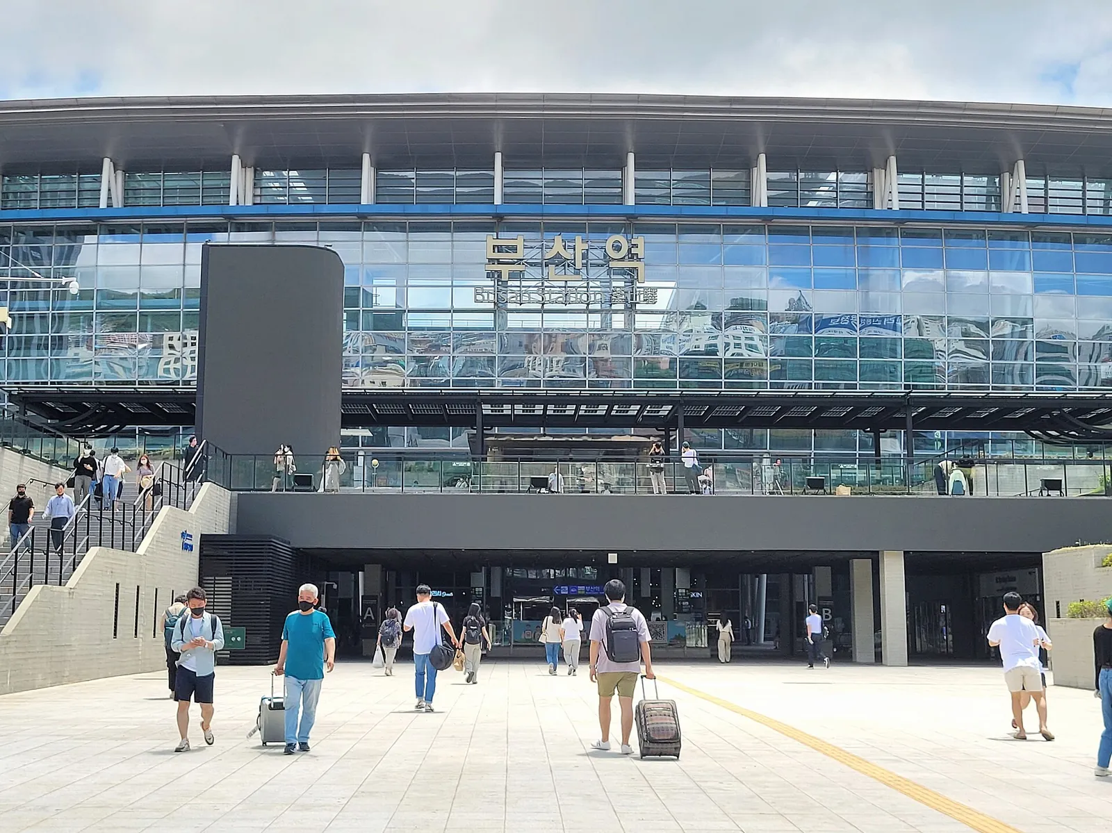 Travellers with luggage crossing the forecourt of Busan Station, the glass-fronted KTX terminal on the Gyeongbu Line